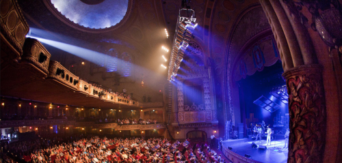 A vibrant theater filled with an audience, illuminated by stage lights during a live performance.