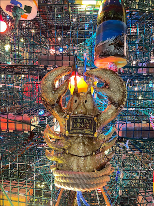 A decorative lobster figure with a sign reading "LOBSTAH KYNZ," surrounded by colorful lights and fishing traps.