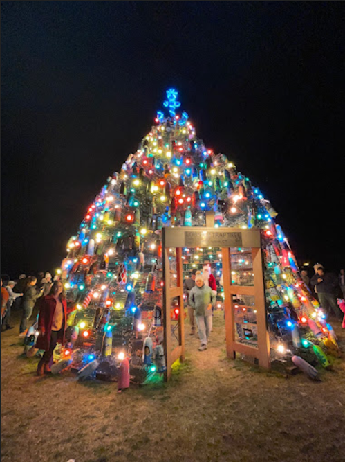 A brightly lit Christmas tree made of colorful lights, with people gathered around it at night.