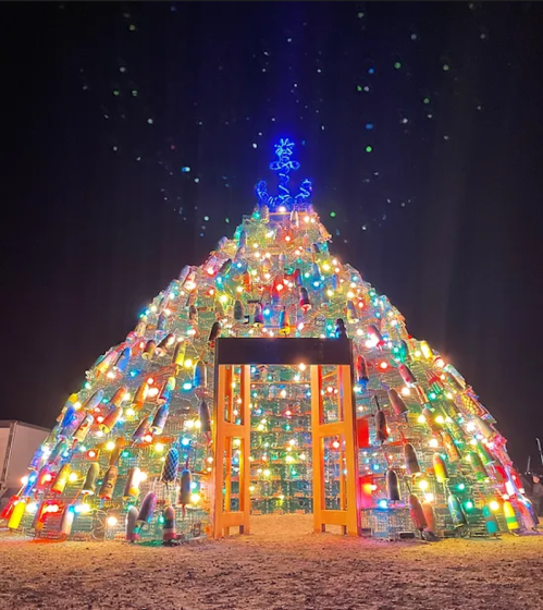 A colorful, illuminated pyramid-shaped structure resembling a Christmas tree, adorned with lights and decorations at night.