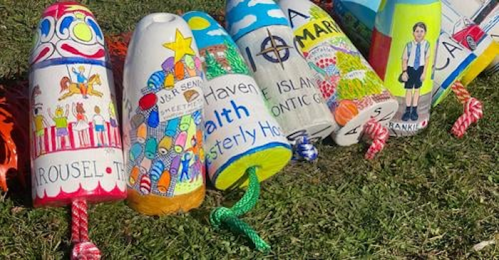 Colorfully painted buoys with various designs and names displayed on grass.