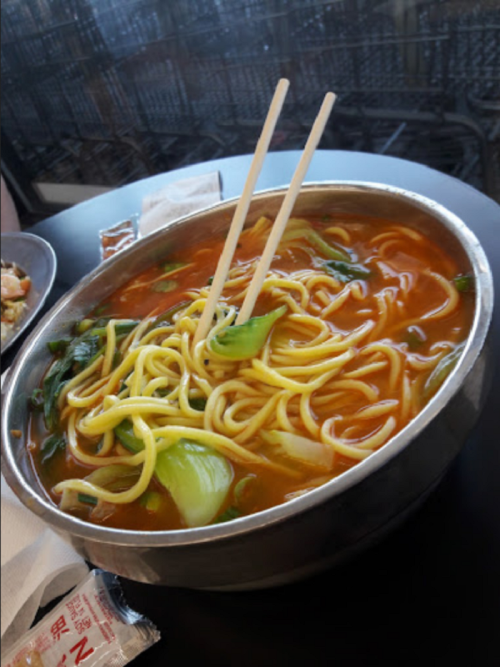A bowl of noodles with vegetables, served with chopsticks, on a table.