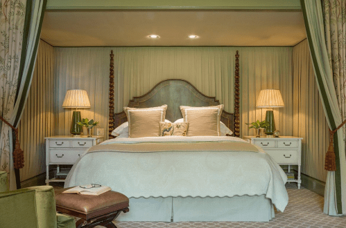 A cozy bedroom featuring a large bed with decorative pillows, two lamps, and elegant curtains in soft green tones.