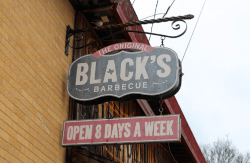 Sign for "Black's Barbecue" with the tagline "Open 8 Days a Week" hanging from a building.