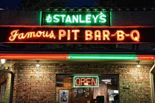 Neon sign for Stanley's Famous Pit Bar-B-Q, glowing "OPEN" at night, showcasing a welcoming barbecue restaurant.