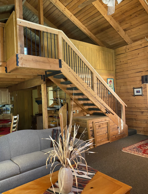 A cozy wooden interior featuring a staircase, a sofa, and a decorative vase on a table.