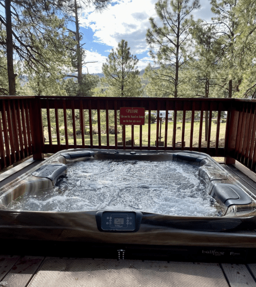 A hot tub on a wooden deck surrounded by trees, with a sign in the background.