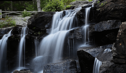 A serene waterfall cascading over dark rocks, surrounded by lush greenery and trees.