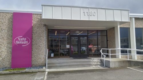 Exterior of Seattle Chocolates building with a pink sign and large glass entrance.