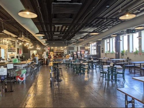A spacious, modern café with tables, chairs, and a counter, featuring large windows and warm lighting.