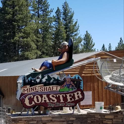 A person enjoys a ride on the Mine Shaft Coaster at Big Bear Lake, surrounded by trees and a clear blue sky.