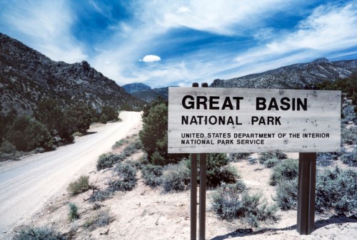 Sign for Great Basin National Park, with a dirt road and mountainous landscape in the background under a blue sky.