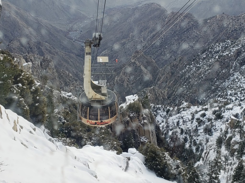 A snow-covered mountain landscape with a gondola cable car traveling through the misty, rugged terrain.