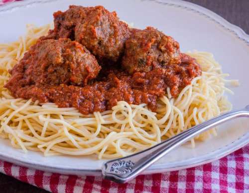 A plate of spaghetti topped with meatballs and marinara sauce, served on a red and white checkered tablecloth.