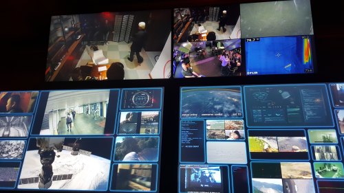 A control room with multiple screens displaying surveillance footage and data from various locations and environments.