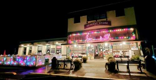 A brightly lit general store at night, adorned with colorful lights and a welcoming outdoor seating area.