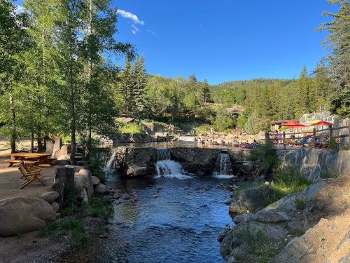 A serene landscape featuring a small waterfall, a stream, and lush greenery under a clear blue sky.