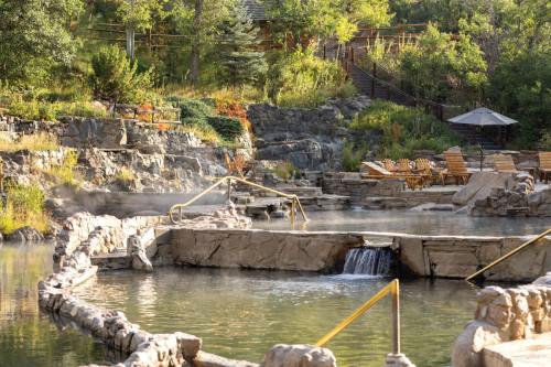 A serene hot spring surrounded by rocks and greenery, with steam rising and wooden loungers nearby.