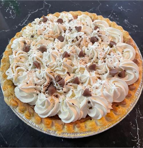A delicious pie topped with whipped cream and chocolate chips, resting on a marble countertop.