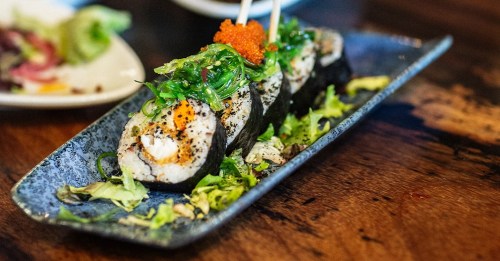 A plate of sushi rolls topped with green seaweed, orange roe, and served on a dark blue dish with lettuce.