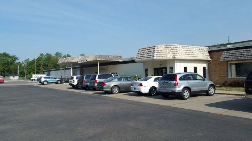 A row of parked cars in front of a low-rise building with a sloped roof and clear blue sky.