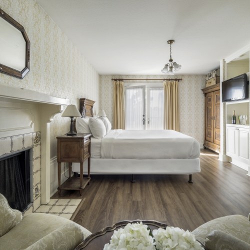 A cozy bedroom with a white bed, wooden furniture, and a decorative fireplace, featuring soft lighting and floral accents.