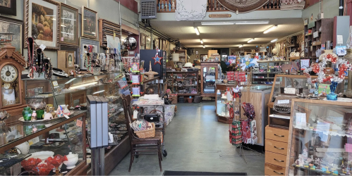 A cozy antique shop filled with glass display cases, vintage items, and decorative pieces along a well-lit aisle.