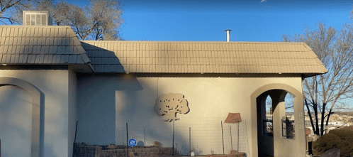 A house with a textured exterior, featuring a tree design on the wall and a sloped roof under a clear blue sky.