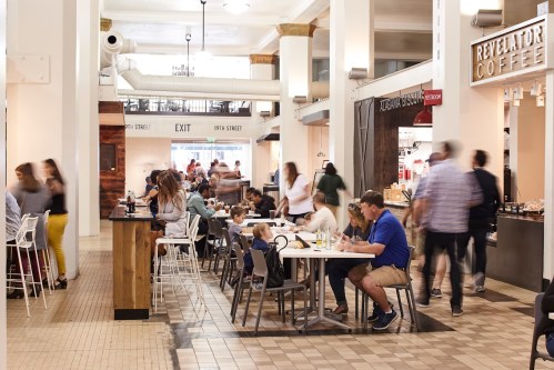 A bustling food hall with people dining, chatting, and enjoying coffee at various tables and counters.