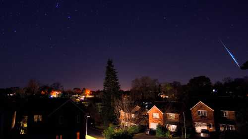 A starry night sky over a suburban neighborhood, with a bright meteor streaking across the scene.