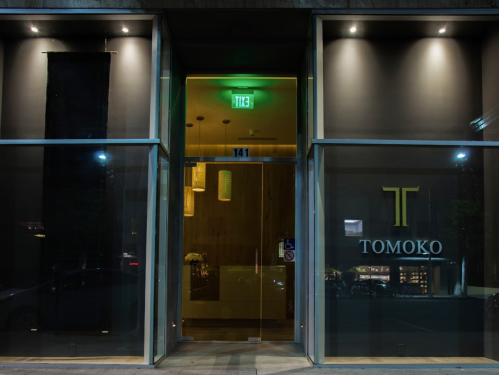 Entrance of Tomoko restaurant at night, featuring a glass door and illuminated signage.