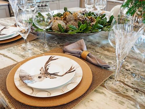 A beautifully set dining table with elegant plates, glasses, and a decorative centerpiece of greenery and natural elements.