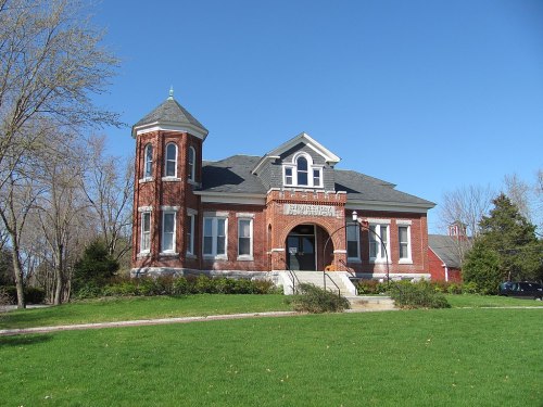 Historic brick building with a tower, surrounded by green grass and trees, under a clear blue sky.