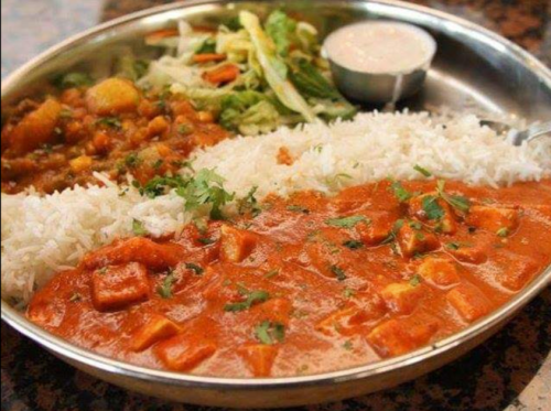 A stainless steel plate with rice, paneer curry, salad, and a small bowl of sauce.