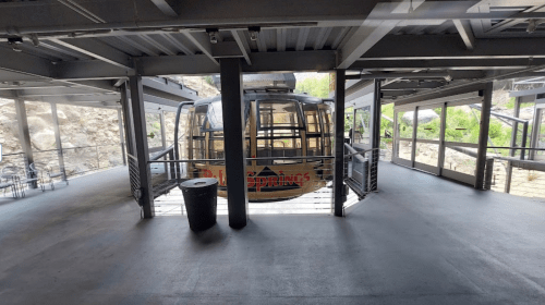 A gondola station with a cable car ready for boarding, surrounded by modern architecture and natural scenery.