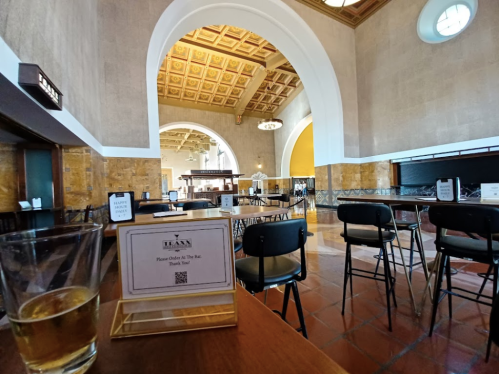 A spacious, empty café with high ceilings, wooden tables, and a glass of drink in the foreground.