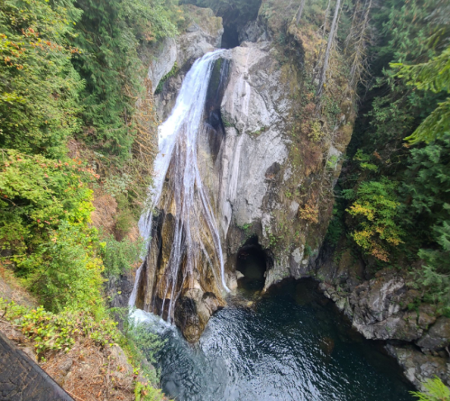 A scenic waterfall cascading over rocky cliffs into a serene pool, surrounded by lush green trees.