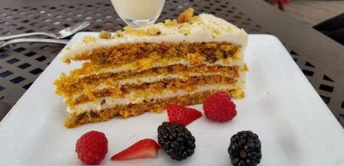 A slice of layered carrot cake with cream cheese frosting, garnished with raspberries and blackberries on a white plate.