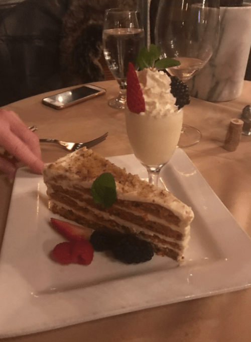 A slice of layered cake with cream, garnished with mint, alongside a dessert cup topped with whipped cream and berries.