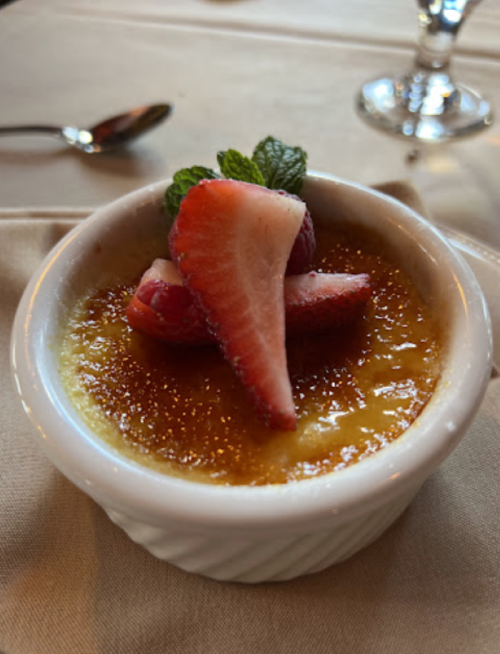 A creamy crème brûlée topped with fresh strawberries and mint, served in a small white dish.