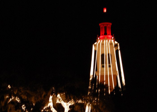 A tower illuminated with red and white lights against a dark night sky.