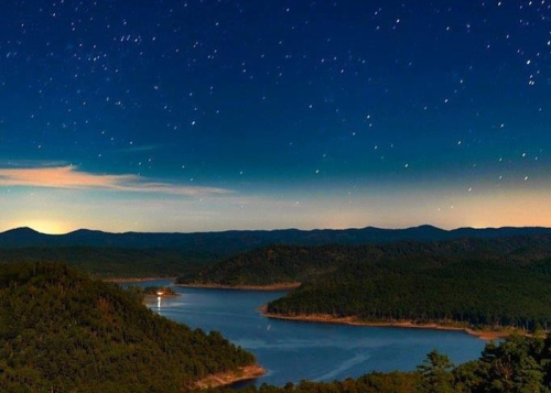 A serene night landscape featuring a lake surrounded by mountains under a starry sky.