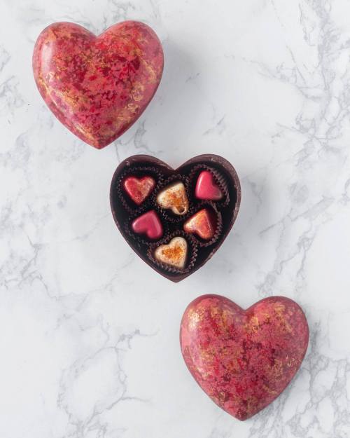 Three heart-shaped boxes on a marble surface, one open revealing assorted chocolates inside.