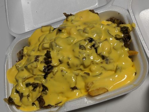 A takeout container filled with fries topped with melted cheese and chopped meat.