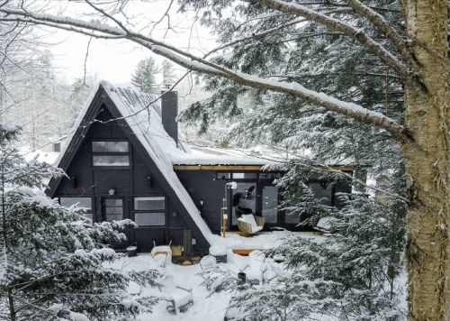 A cozy A-frame cabin surrounded by snow-covered trees in a winter landscape.