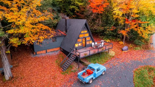 A cozy A-frame cabin surrounded by vibrant autumn foliage and a vintage blue truck parked nearby.