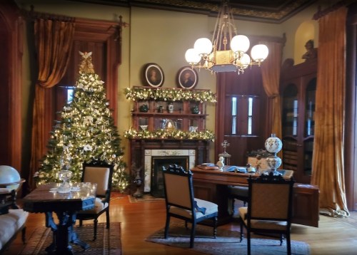 A cozy room decorated for the holidays, featuring a Christmas tree, fireplace, and elegant furniture.