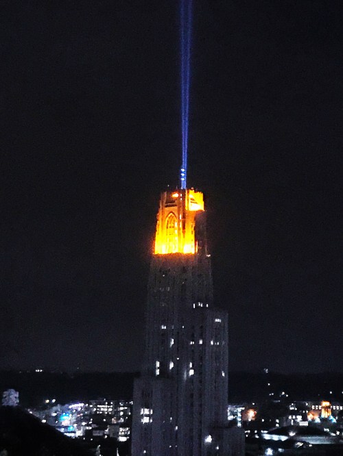The Empire State Building illuminated in orange with a blue beam of light shining into the night sky.