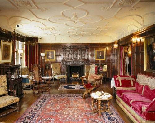 A vintage living room with ornate wood paneling, elegant furniture, and classic portraits on the walls.