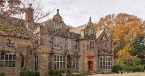 Historic stone mansion surrounded by autumn trees and a cloudy sky.